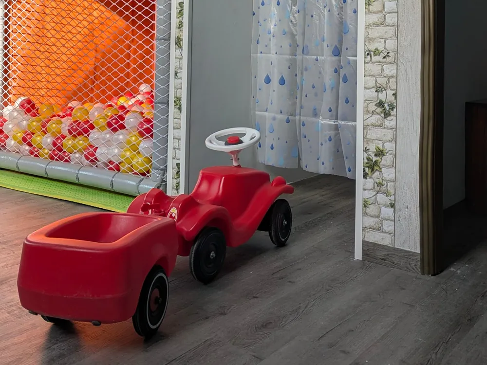 Rotes Rutschauto mit Anhänger vor Bällebad und Spielhaus